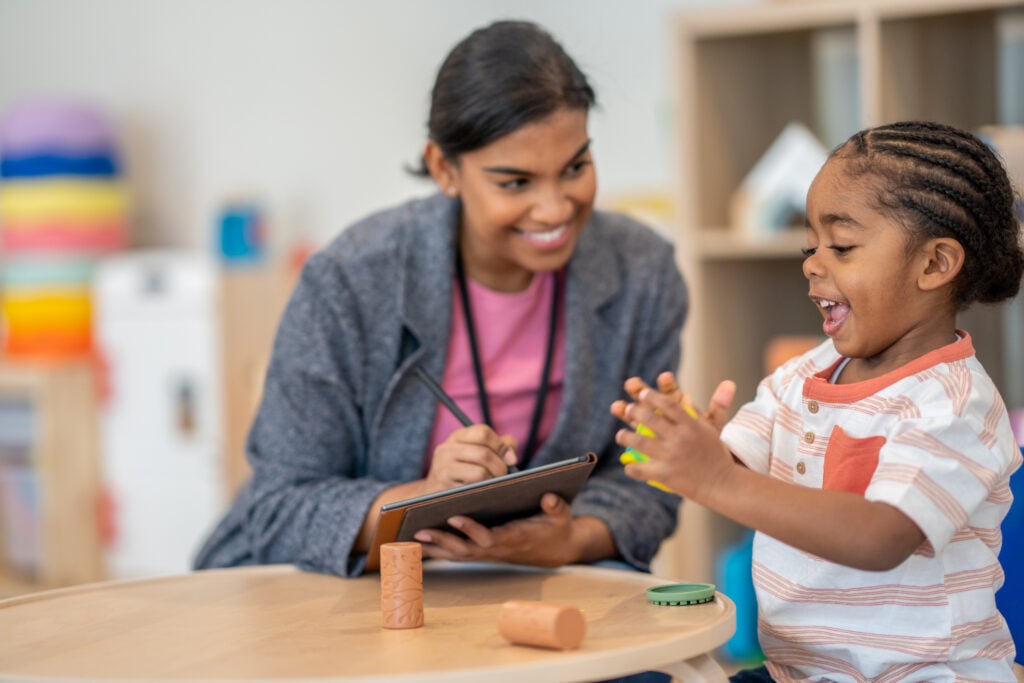 A female Occupational Therapist works with a young mixed race boy during a therapy session. She is using Play-Doh to work on the boys gross motor skills.