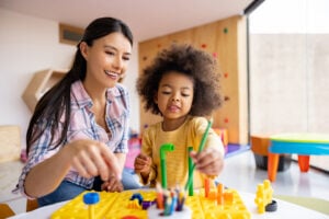 Happy Latin American teacher playing with an African American girl in the classroom
